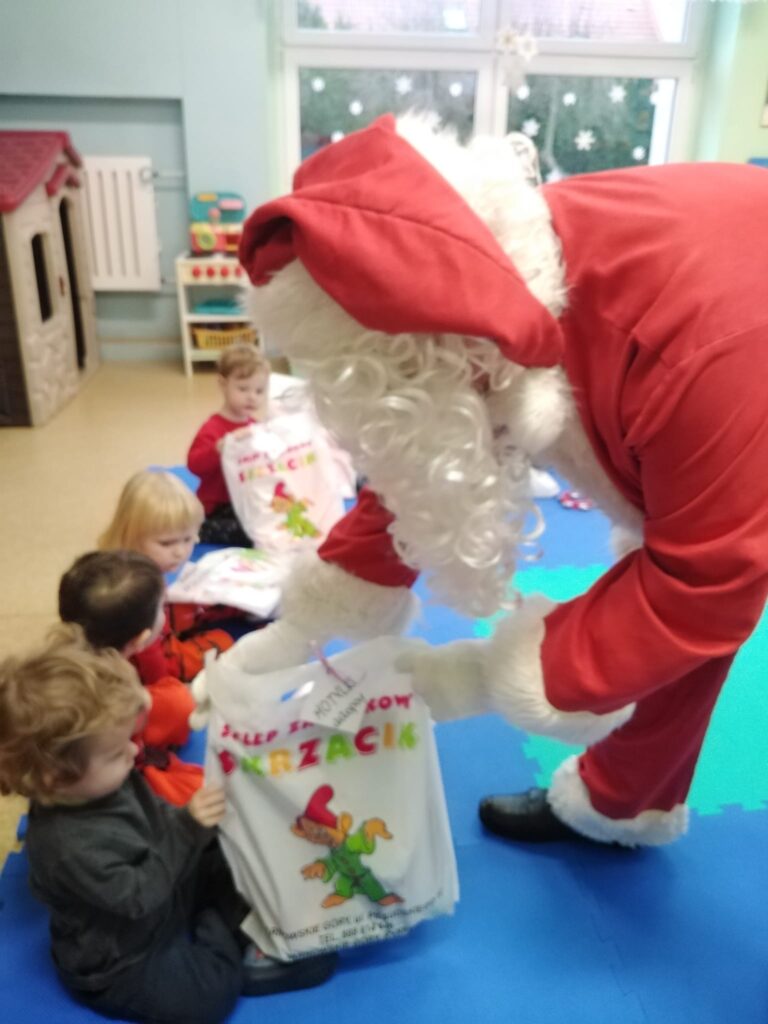 Mikołaj rozdaje dzieciom siedzącym na dywanie prezenty